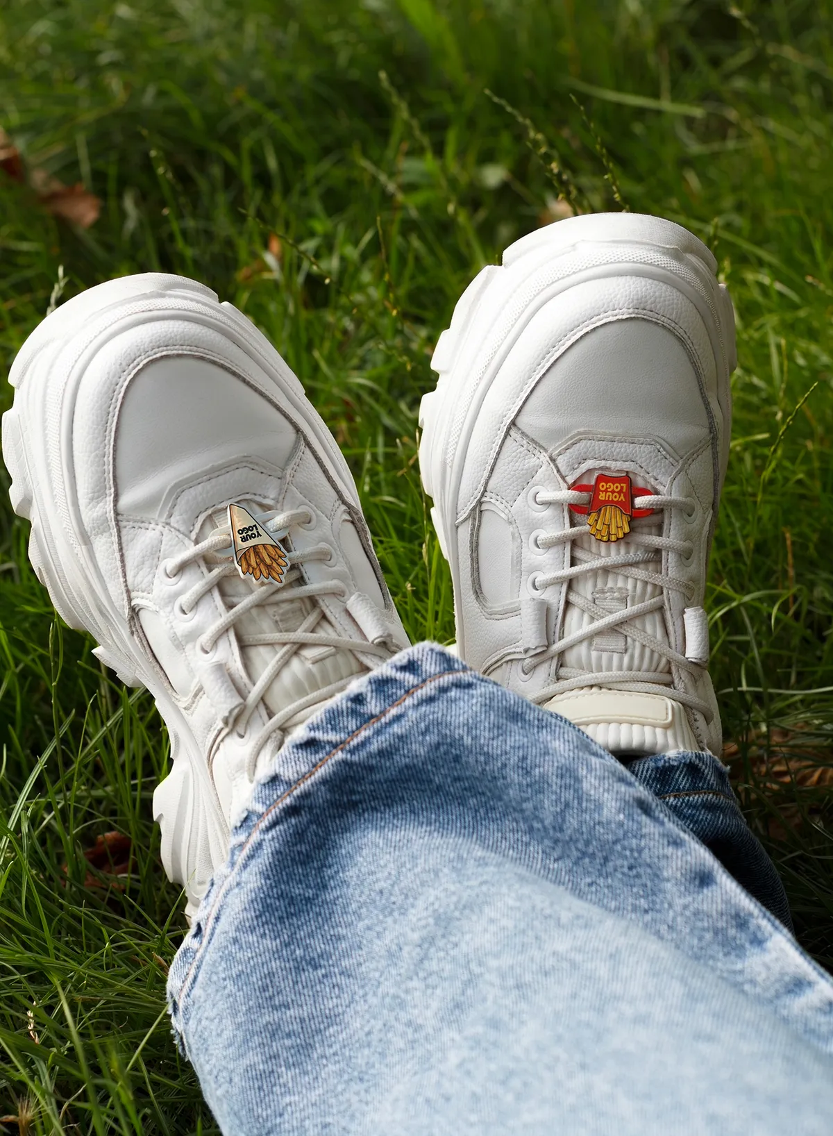 Nakładki na sznurówki w kształcie frytek na białych sneakersach na trawie