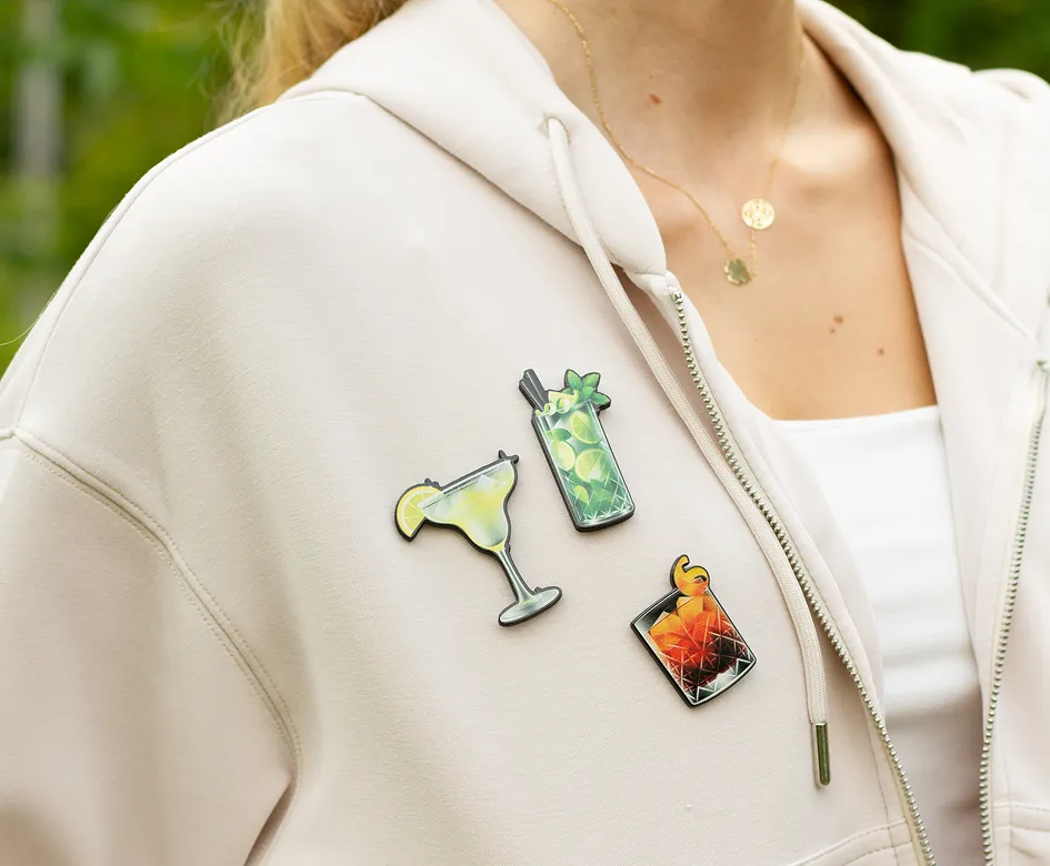 Trzy piny w kształcie drinków przypięte do beżowej bluzy