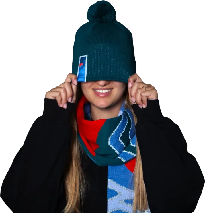 Girl wearing a green pom-pom hat with a patch, pulled down over her eyes, and a scarf with reflective waves