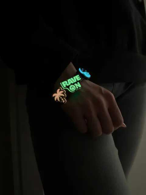 Bransoletka FLUO na nadgarstku ze świecącymi przypinkami: napis RAVE ON, palma i niebieski element