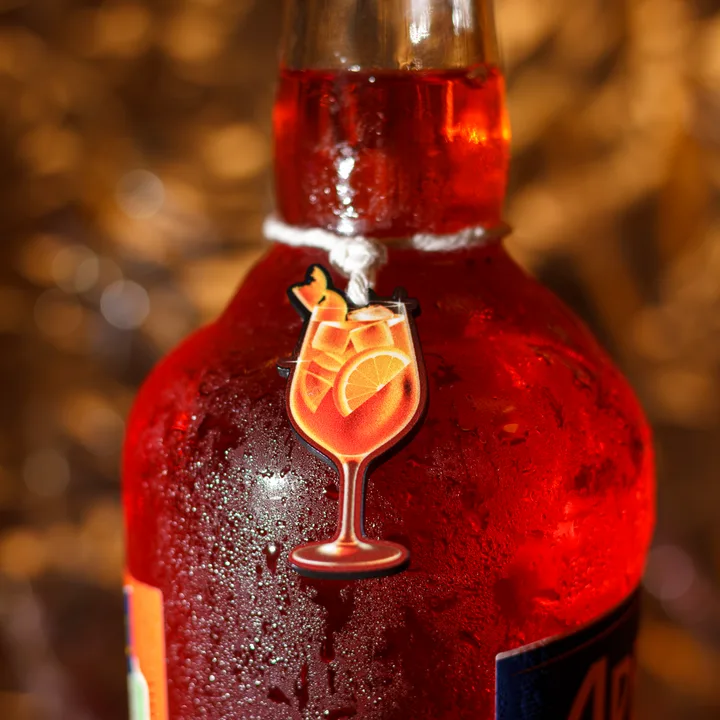 Zawieszka w kształcie kieliszka spritz na białym sznurku zawiązanym na szyjce czerwonej butelki